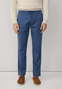 Pantalones azules hechos de una tela suave, con una cintura elástica y cordón ajustable, y piernas rectas. Combinados con calzado marrón.