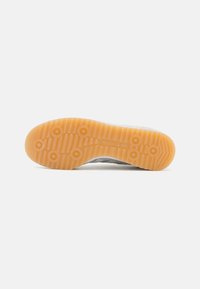 Suela de zapato Adidas, con un caucho naranja texturizado que presenta patrones de tracción circulares y un logotipo en relieve, presentado sobre un fondo blanco.