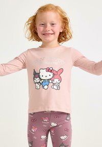 Maglietta a maniche lunghe rosa con grafica di Hello Kitty e dei suoi amici; abbinata a leggings rosa decorati con motivi di Hello Kitty.