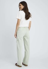 Pantalons cargo vert clair avec deux poches arrière et une poche sur le côté, assortis à un t-shirt blanc court. Tissu lisse et coupe décontractée.