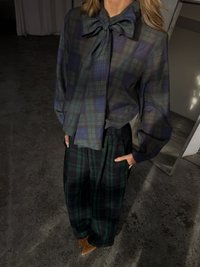 Plaid blouse in dark green and navy with a bow tie collar, paired with loose-fitting plaid trousers in dark green and navy, and beige pointed shoes.