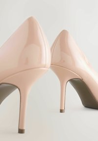 Lichtroze lakleren pumps met een spits toelopende neus en naaldhak, met een gladde textuur en subtiele stikdetail.