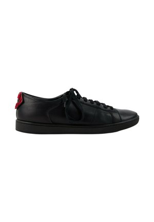 Sort læderlavsko sneaker med sorte snørebånd og en rød detalje på hælen, vist fra siden på en hvid baggrund.