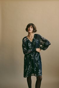 Abito nero a fiori con maniche lunghe e trasparenti e scollatura a V. Presenta una vita aderente e una gonna fluente, lunga fino al ginocchio, con eleganti accenti floreali bianchi.