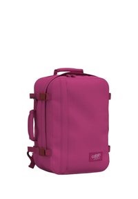 Fuksia matkakassi, jossa on suorakulmainen muoto, yläponnari, sivuponnarit ja säädettävät hihnat. Vetoketjusuljenta, logo edessä.