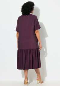 Violetti midi-mekko, jossa on lyhyt hihansuu, tekstiiliraekuvio, kerätty helma ja löysä muotoilu, yhdistettynä keltaisiin remmikorkokenkiin.