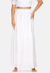 Biała maxi spódnica z lekkiego materiału, z wycięciami w kształcie oczek, elastycznym pasem i warstwowym krojem. Łączona z krótkim, obcisłym topem.