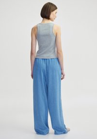 Grijze mouwloze top gecombineerd met lichtblauwe denim broeken met wijde pijpen. De outfit heeft een casual snit en een gladde stofstructuur.