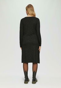 Schwarzes, langärmliges Kleid mit geradem Schnitt, strukturiertem Stoff mit metallischen Einsprengseln, kombiniert mit schwarzen Knöchelboots und transparenten Strumpfhosen.