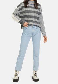 Grå och vit randig stickad tröja med hög hals, matchad med ljusblå rakben-jeans och krämfärgade snörstövlar.