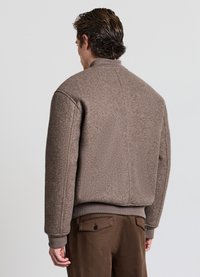 Braune, strukturierte Woll-Bomberjacke mit geripptem Kragen und Bündchen; sichtbare Nahtdetails; kombiniert mit brauner Hose.