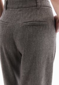 Grijze herringbone broek met een getailleerde pasvorm, subtiele textuur en dubbele achterzakken met fijne stikselaccenten.