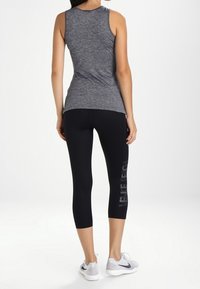 Top atletico senza maniche grigio abbinato a leggins neri lunghi fino al polpaccio, con un motivo grafico lucido di lato. Le scarpe sono argento con dettagli neri.
