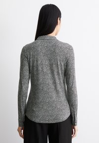 Langärmliges Hemd in einem schwarz-weißen Tiermuster, das einen Kragen und Knopfdetails an den Manschetten aufweist. Weicher, glatter Stoff mit einer taillierten Passform.