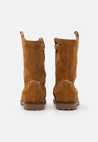 Ein Paar braune Wildleder-Stiefel bis zur Wade, von hinten betrachtet, mit Zuglaschen und Gummisohle auf einem weißen Hintergrund.