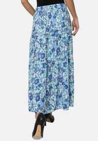 Jupe maxi florale avec taille smockée, présentant des couleurs bleu, vert et blanc. Tissu léger avec un design à volants et une coupe longueur cheville.