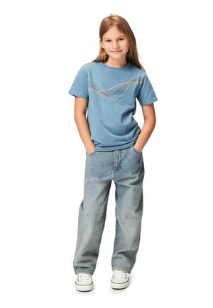 Blå bomulds t-shirt med multicolor bølgedesign, parret med baggy lyse denim jeans og hvide sneakers.