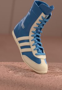 High-top sneaker in blue leather with cream accents, featuring three side stripes, a rounded toe, and flat laces. Textured sole.