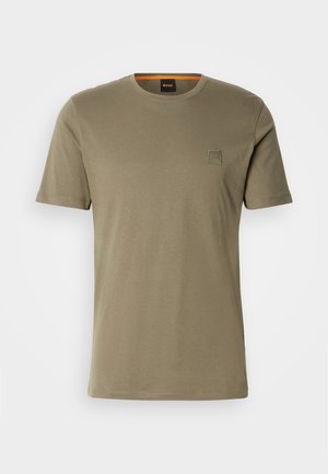 Tricou scurt din bumbac, de culoare verde măslinie, cu guler rotund și un mic patch cu logo pătrat pe pieptul stâng. Textură netedă.