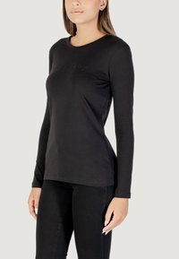 Schwarzes Langarmshirt aus weichem Material, mit rundem Halsausschnitt und dezent geprägtem Text auf der Brust. Figurbetonter Schnitt, glatte Textur.