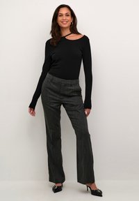Zwarte lange mouw top met een asymmetrische halslijn, gecombineerd met grijze streepjestrapants en zwarte puntige hakken.