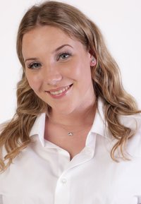 Zilveren sieraden bevatten een centrale heldere stenen hanger en bloemstudoorbellen. Het model draagt een witte blouse met knopen en een kraag.