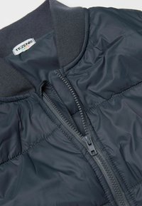 Námořnický prošívaný péřový kabát, zapínání na zip, žebrovaný límec, lehká syntetická tkanina, hladká textura, prošívané detaily.