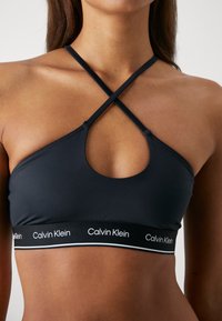 Top sportivo nero con design a chiave, spalline incrociate e fascia con logo bianco. Realizzato in tessuto liscio ed elasticizzato.