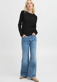 Maglione nero a maniche lunghe con scollatura rotonda, abbinato a jeans ampi di un leggero blu. I jeans hanno una texture sbiadita e cuciture visibili.