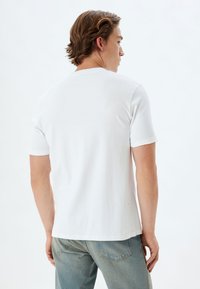 Hvid bomulds T-shirt med korte ærmer, rund halsudskæring og en afslappet pasform, parret med lyseblå denim jeans. Glat tekstur og enkelt design.