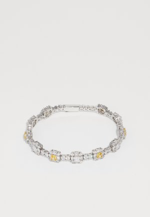 Zilverkleurige armband met afwisselend grote heldere en kleine gele edelstenen, met een geometrisch ontwerp en een veilige sluiting.