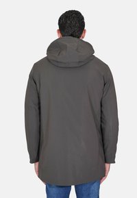 Giacca con cappuccio di colore grigio scuro con una texture liscia, caratterizzata da un taglio lungo e dettagli di cuciture sottili. Indossata sopra jeans blu.