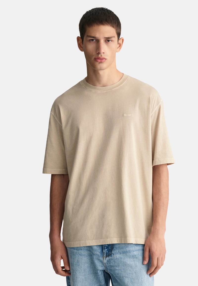 Camiseta corta de manga corta color beige hecha de algodón, con cuello redondo y un pequeño logo en el pecho, combinada con jeans de color azul claro.