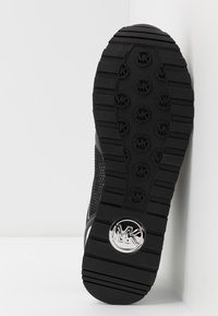 Semelle de chaussure en caoutchouc noir avec motif d'adhérence texturé, comportant des accents de logo circulaire et un bord courbé, montrant la profondeur et les détails de construction.