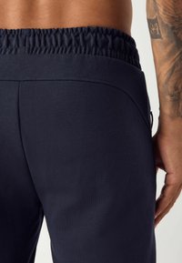 Pantalones de chándal en navy con cintura elástica, textura suave, bolsillos laterales y corte ajustado. Costuras visibles y detalles de diseño minimalistas.