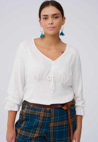 Witte blouse met lange mouwen, een V-hals en geraffineerde details, met een trekkoord in de taille. Gemaakt in combinatie met blauw-orange geruite broek.