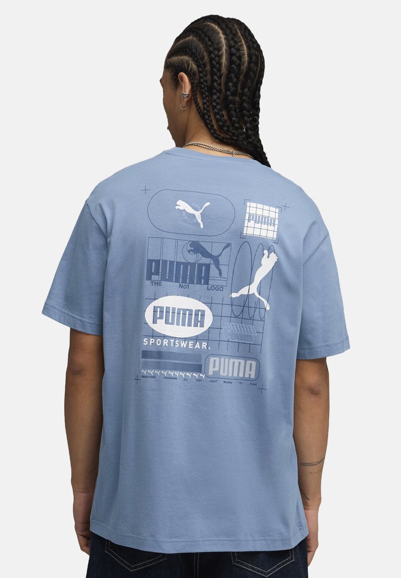 Tricou din bumbac de culoare albastru deschis, cu diverse imprimeuri, inclusiv logo-uri și texte, pe spate. Croială lejeră, mâneci scurte și guler rotund.