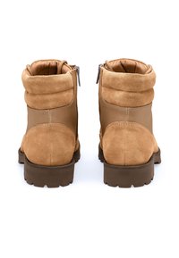 Brune ruskindsankelstøvler med en opsmøget manchet, sidelommer med lynlåse og en robust gummisål. Glat tekstur og enkelt design.