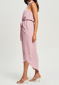 Rosa ärmelloses Kleid aus strukturiertem Stoff, tailliert, mit vorderem Bindedetail, hoch-tiefem Saum und glatten Sandalen.