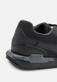 Schwarzer Sneaker mit einer strukturierten Mesh-Oberfläche, glatten Lederakzenten und einer klobigen, transparenten Gummisohle mit Belüftungsdetails.