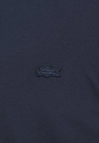 Mörkblå texturerad polo skjorta i bomull, med en broderad svart krokodil-logotyp på vänster bröst.