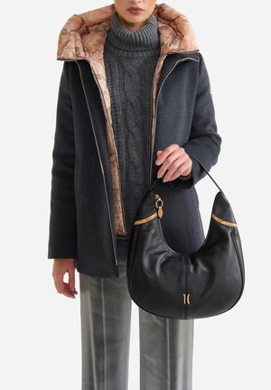 Borsa hobo in pelle nera con dettagli dorati, forma curva, superficie texturizzata. Abbinata a un cappotto scuro con fodera chiara e con motivo.