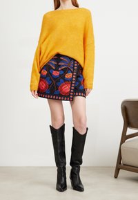 Överdimensionerad gul tröja, figurnära svart mini-kjol med färgglad blommönster, och knähöga svarta läderstövlar.