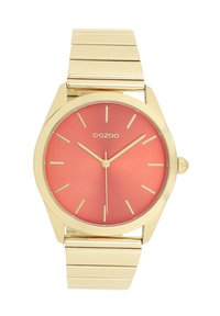 Montre à bracelet en métal doré avec un boîtier rond, dotée d'un cadran mat corail et d'index en or. Marque "OOZOO" affichée sur le cadran.