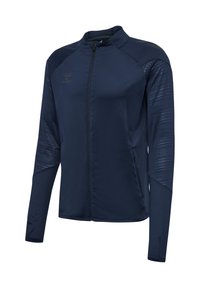Veste de sport bleu marine avec fermeture éclair intégrale, manches texturées, col montant, poches latérales et logo discret sur la poitrine.