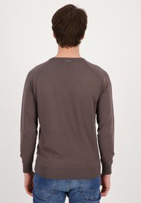 Maglione grigio con maniche lunghe, scollatura rotonda, orlo e polsini a costine, con un discreto dettaglio del logo sul retro. Indossato con jeans blu.