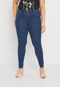 Smal blå denimjeans med medelhavsvask, fem fickor och knappstängning. Bärs med beige blockklackssandaler.