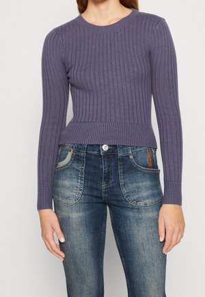 Pull en maille côtelée violette avec un col rond et des manches longues, associé à un jean bleu délavé avec des poches avant et des détails en délavage léger.