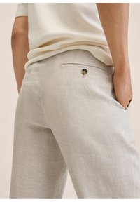 Jasnobeżowe lniane spodnie o luźnym kroju i gładkiej fakturze, z tylną kieszenią ozdobioną okrągłym guzikiem.