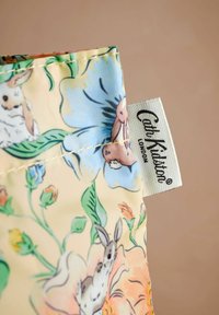Pouch od cvjetnog materijala s pastelnom pozadinom na kojoj se nalaze zečevi i šarene cvjetove. Uključuje bijelu etiketu s natpisom "Cath Kidston London".